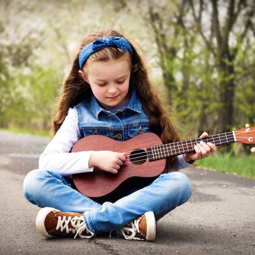 Pretty young girl playing ukulele in the park